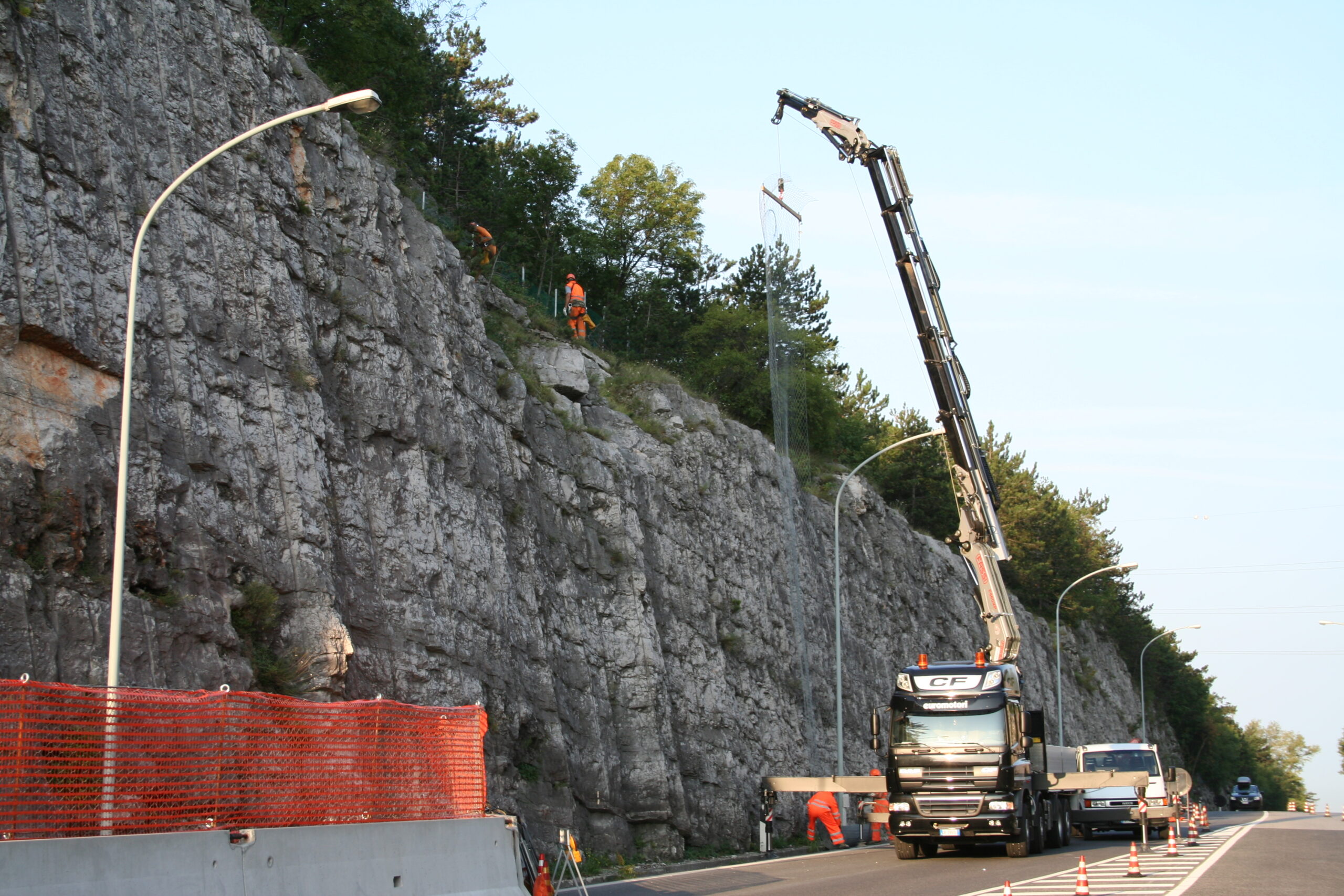 Operai appesi su corda che disgaggiano una parete franosa a bordo autostrada