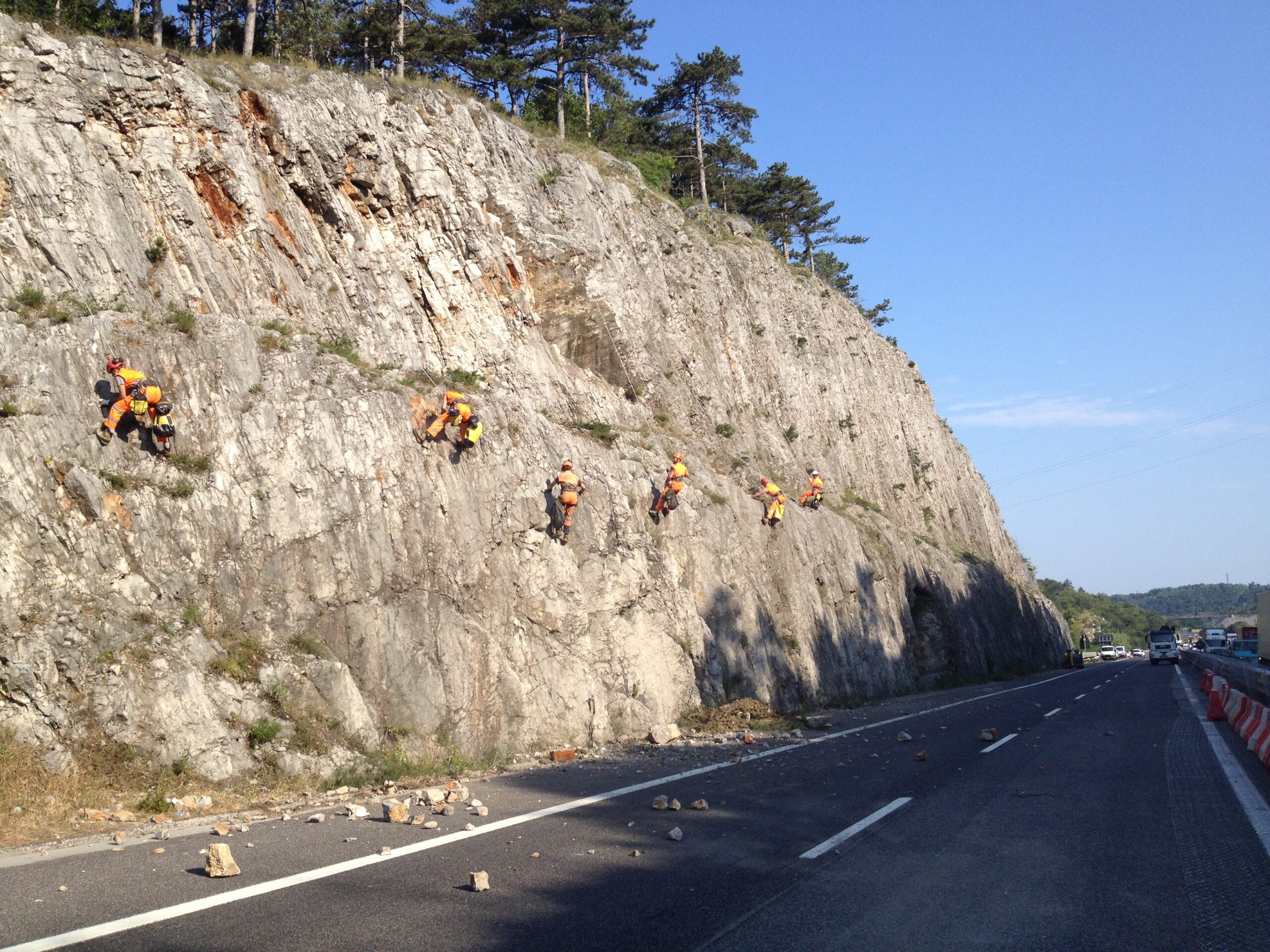 Operai appesi su corda che disgaggiano una parete franosa a bordo autostrada